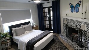 A bedroom with a bed, a ceiling fan, a fireplace, and a window with curtains.