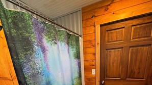 Een badkamer met een houten deur, een douchegordijn met een natuurlandschap en een houten vloer.
