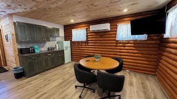 Cocina compacta con armarios de madera, un refrigerador y un microondas. Hay un comedor con una mesa redonda y dos sillas.