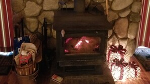 Un camino in pietra con un camino, un cesto di legna da ardere e un piccolo tavolino con un libro.