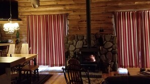 Interno di una baita in legno con camino in pietra, pareti di legno e una testa di cervo appesa al muro.