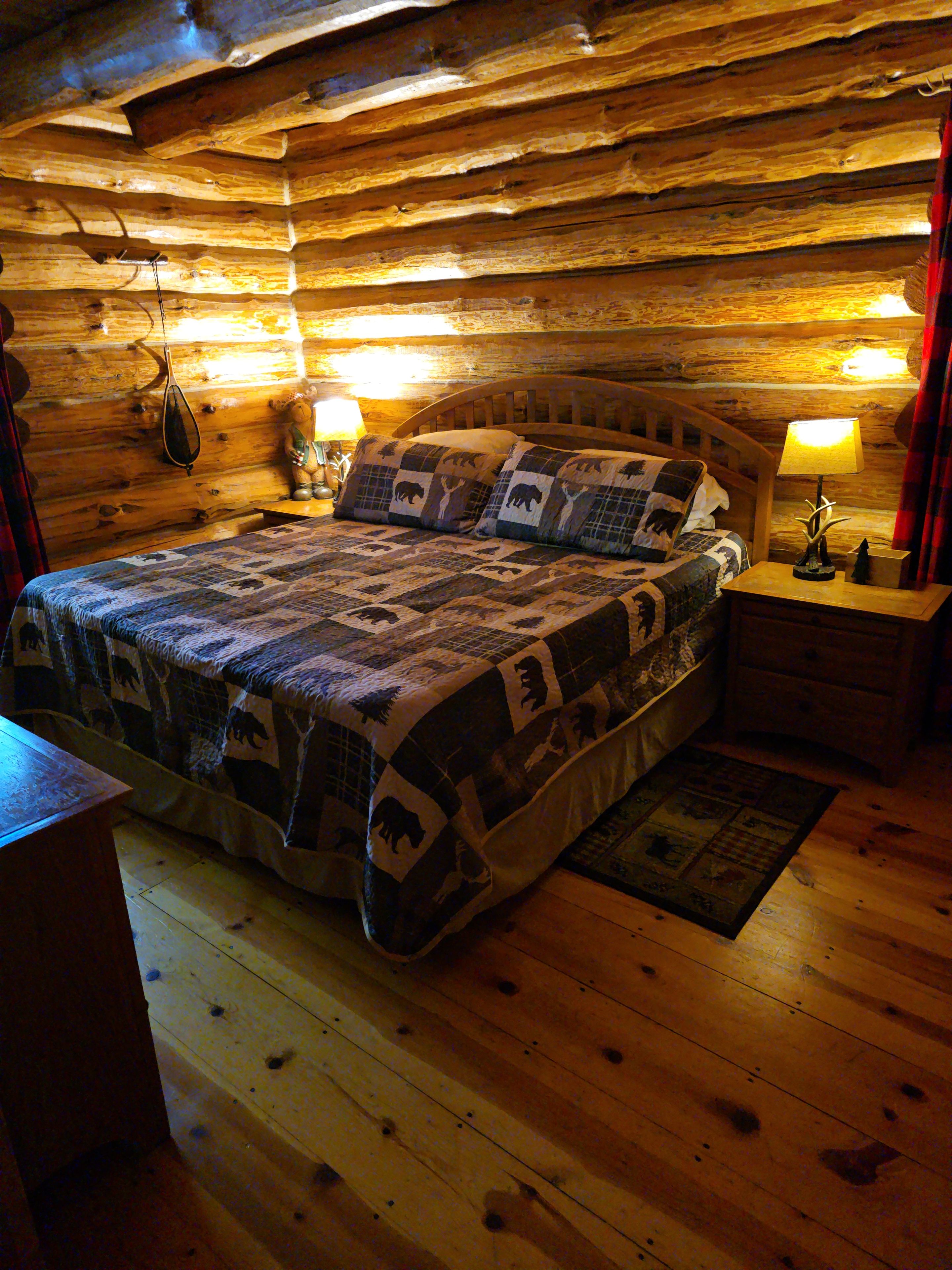Une chambre dans un chalet en rondins, avec un lit en bois, deux lampes de chevet et une table de chevet en bois.