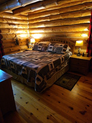 A log cabin bedroom with a wooden bed, two bedside lamps, and a wooden nightstand.