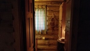 Un stretto corridoio in legno che conduce a una stanza con tenda a scacchi e un anello luminoso appeso.