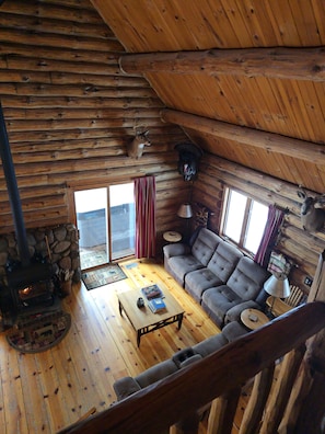 A log cabin interior with a stone fireplace, a sofa, a coffee table, and a dog mounted on the wall.
