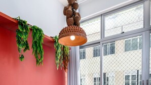 A dining area with a round table set for four, wooden chairs, a hanging light fixture, and a view of a building through large windows. - For Families 10 Minutes From Ipanema Beach Ns103 (Rio de Janeiro)