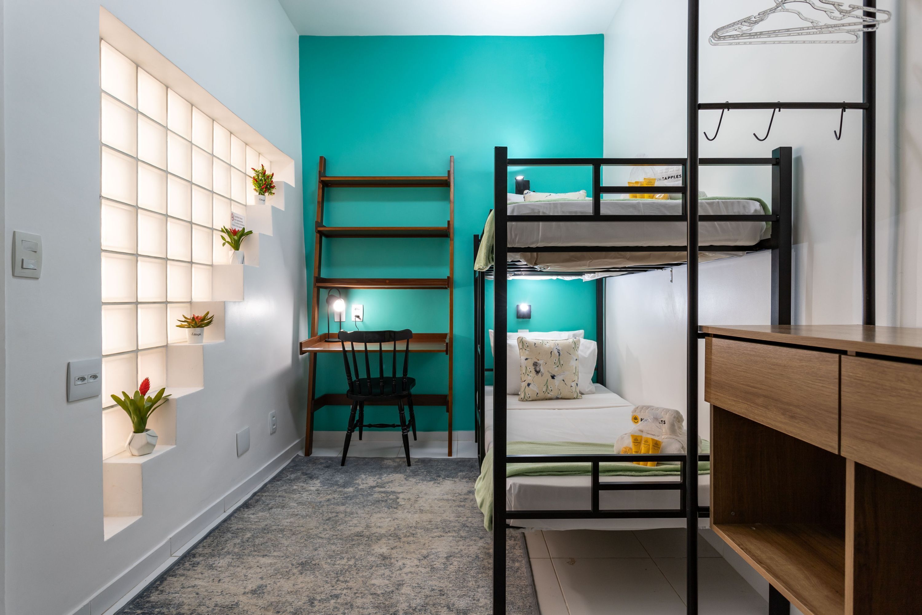 A compact room with a bunk bed, a desk with a chair, and a shelving unit with plants.