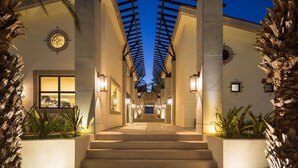 Una entrada de hotel moderna y bien iluminada, con una escalera central rodeada de palmeras y columnas arquitectónicas.