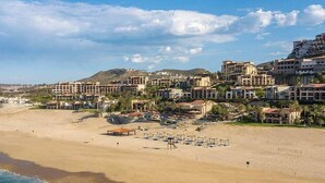Un complejo turístico frente al mar, con villas en la playa, una playa de arena y un paisaje montañoso de fondo.