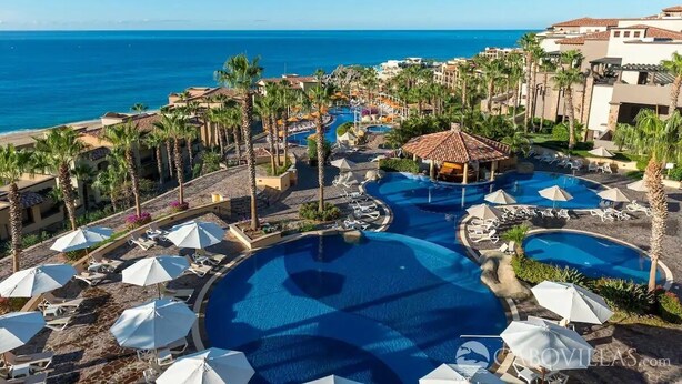Un resort con varias piscinas, palmeras y vistas al océano.