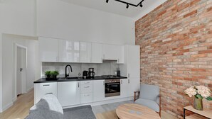A modern kitchen with white cabinets, a brick wall, and a dining area with a round table and chairs. - Forma by Grand Apartments (Sopot)