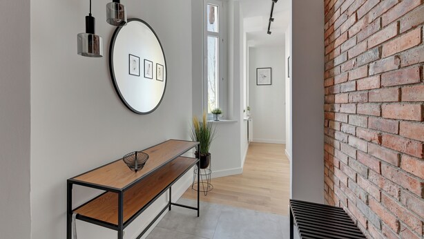 A hallway with a wooden bench, a round mirror with framed pictures, and a brick wall. - Forma by Grand Apartments (Sopot)