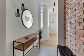 A hallway with a wooden bench, a round mirror with framed pictures, and a brick wall. - Forma by Grand Apartments (Sopot)