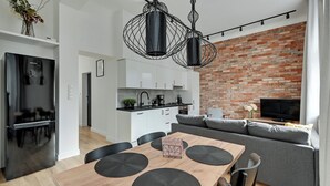 A modern kitchen with white cabinets, a brick wall, and a dining area with a wooden table and black placemats. - Forma by Grand Apartments (Sopot)