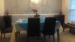Un coin repas avec une nappe bleue, des chaises, une horloge et un vase rempli de fleurs.