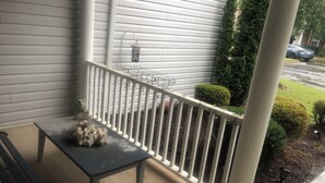 Une véranda avec un banc, une balustrade et un petit espace jardin, avec une voiture garée au fond.