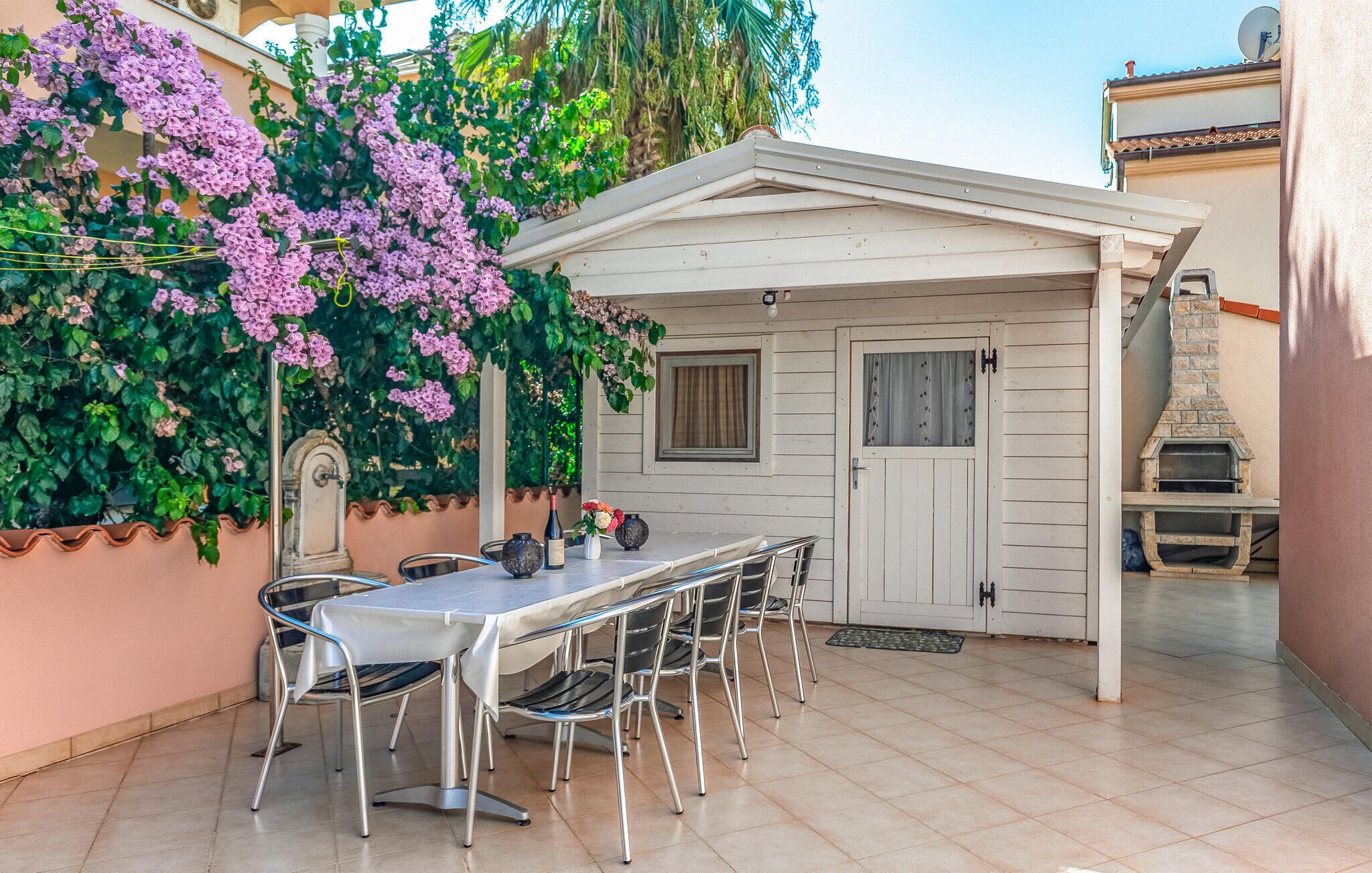 Un patio al aire libre con mesa y sillas, un horno de ladrillo y una pared cubierta de flores moradas.