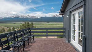 A wooden deck with metal chairs, a view of snow-capped mountains, and a building with a dark exterior and white windows. - Sweet Dreams -MtnViews & Hot Tub (Leadville)