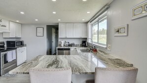 A modern kitchen with white cabinets, a marble countertop, and a large window. - Sweet Dreams -MtnViews & Hot Tub (Leadville)