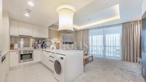 A modern kitchen with a built-in washing machine, a dining area with a table, and a large window with curtains. - Holistay Luxury Homes,  Down Town Direct Access Dubai Mall (Dubai)