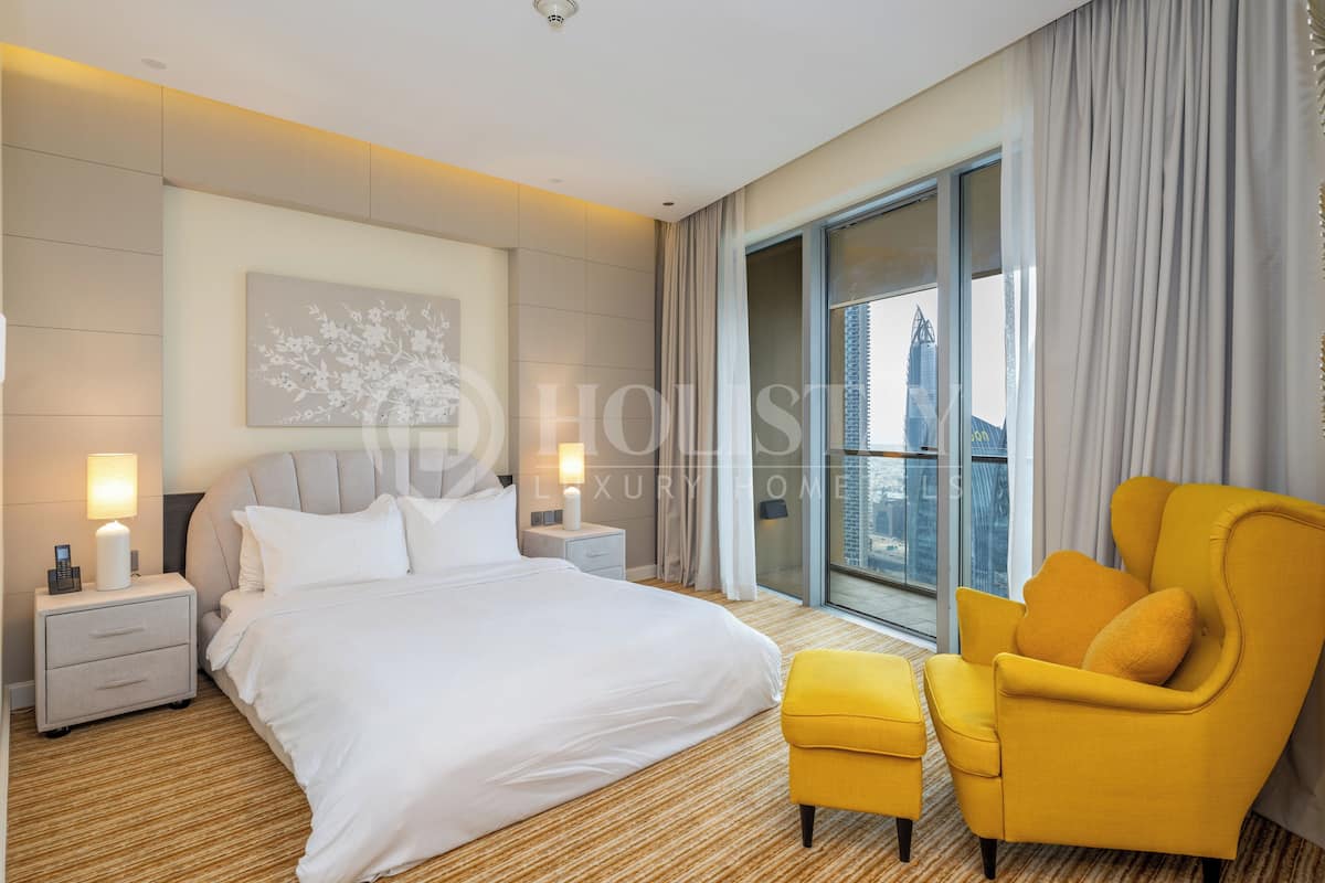 A modern hotel room with a large bed, a yellow armchair, and a city view through the window.