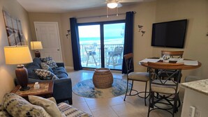 A living room with a sofa, chairs, a coffee table, a TV, and a balcony with a view.
