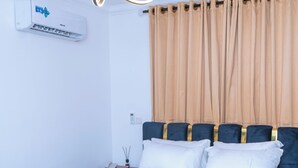 Un dormitorio con cama, cortinas, un equipo de aire acondicionado e iluminación empotrada.