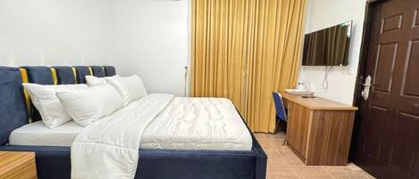A bedroom with a bed, a desk, a chair, a TV, and a door.