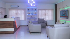 Una moderna zona de recepción con un mostrador de madera, un área de estar central con dos sofás y un estante en la pared con objetos decorativos.