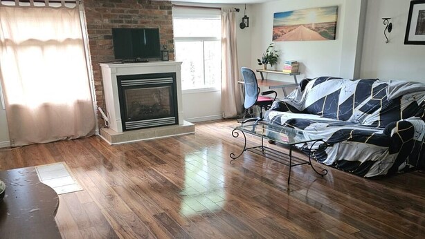 A living room with a fireplace, wooden flooring, a sofa, and a television. - Charming 2-bedroom cottage in Bancroft with AC, WiFi. Enjoy your stay (Bancroft)