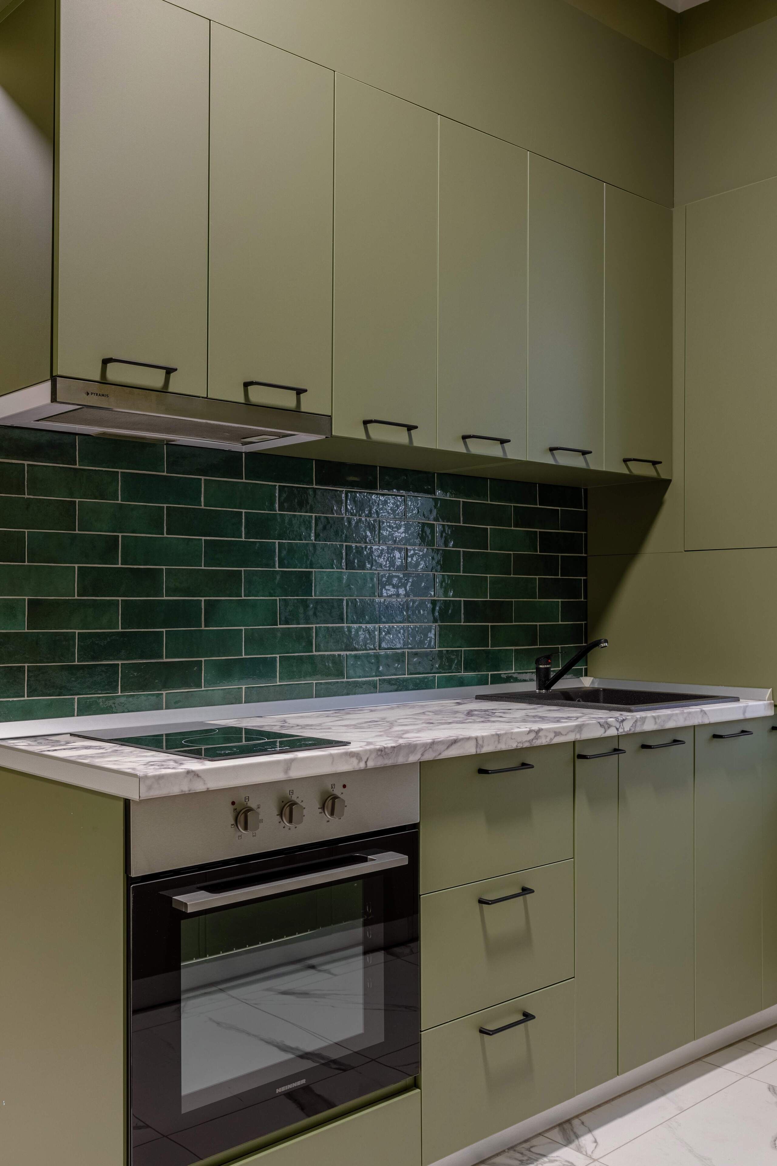 A kitchen with green cabinets, a black oven, and a tiled backsplash.