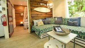 A cozy room with a bed, a table with a basket, and a wall-mounted surfboard. - Mini Up House (Cahuita)