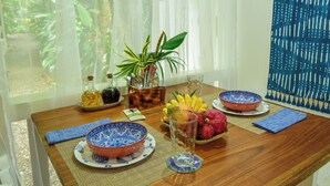 A dining table with blue and white patterned bowls, a glass of water, a fruit bowl, and a potted plant. - Mini Up House (Cahuita)