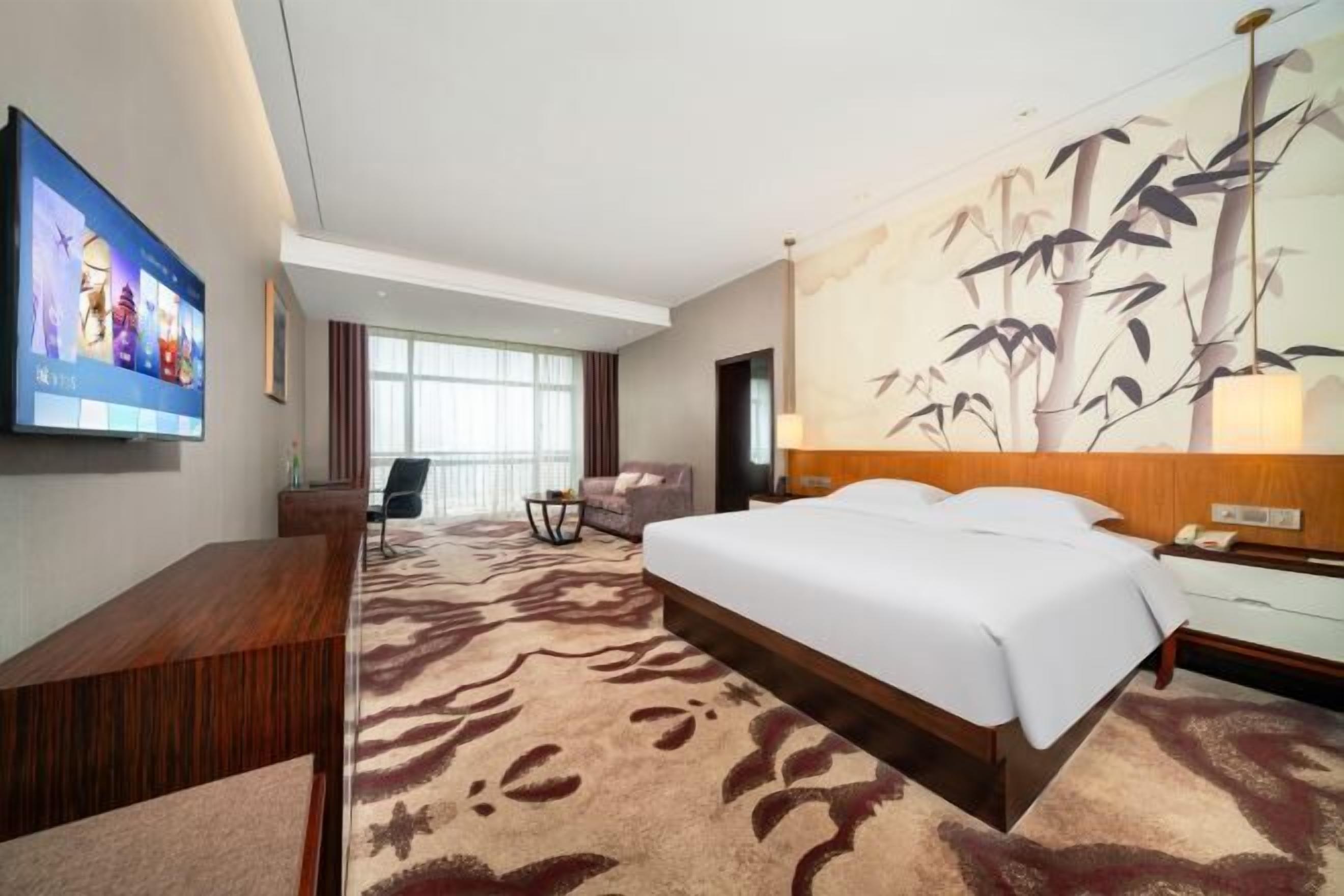 Ein Hotelzimmer mit einem großen Bett, einem Flachbildfernseher, einem Schreibtisch, einem Sessel und einem großflächigen Wandbild.