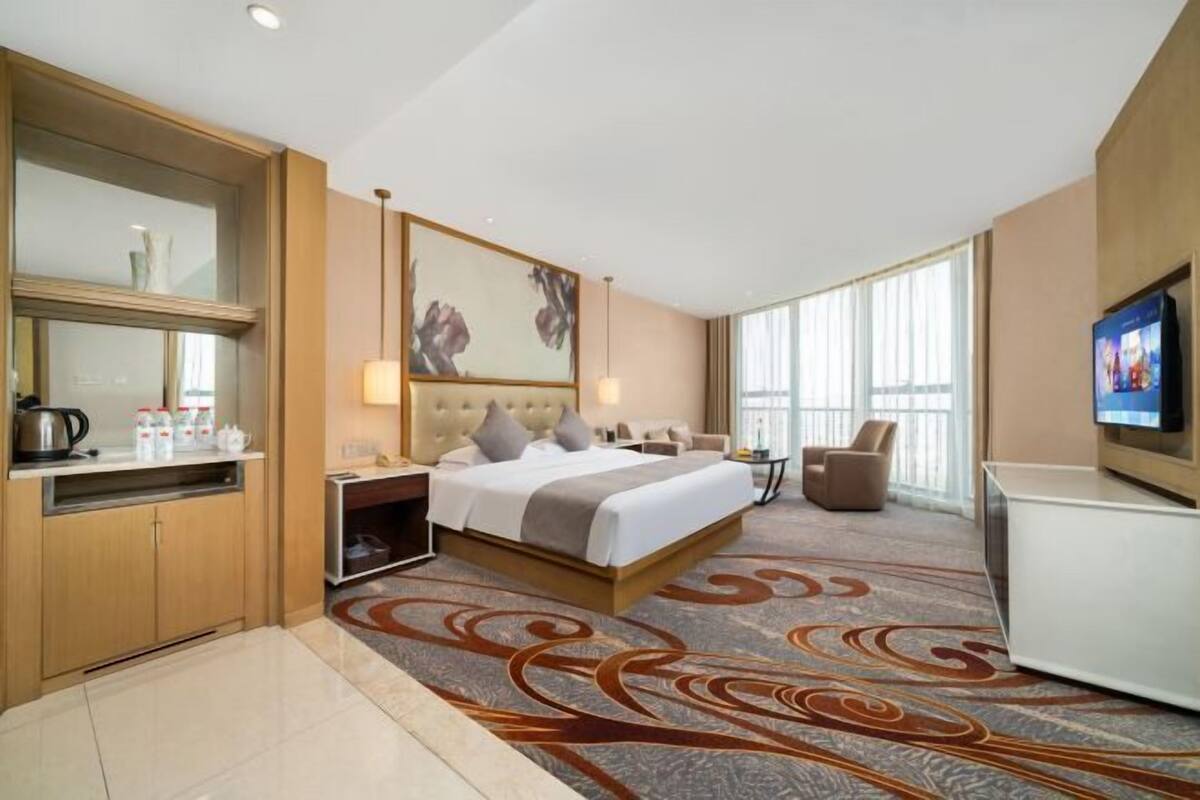 Habitación de hotel con cama, mesita de noche, lámpara, televisor y vistas a la ciudad.