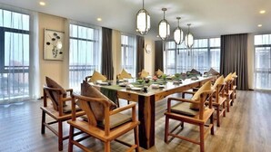 Un vaste espace dédié à la salle à manger, avec une longue table en bois, de nombreuses chaises et des luminaires suspendus.