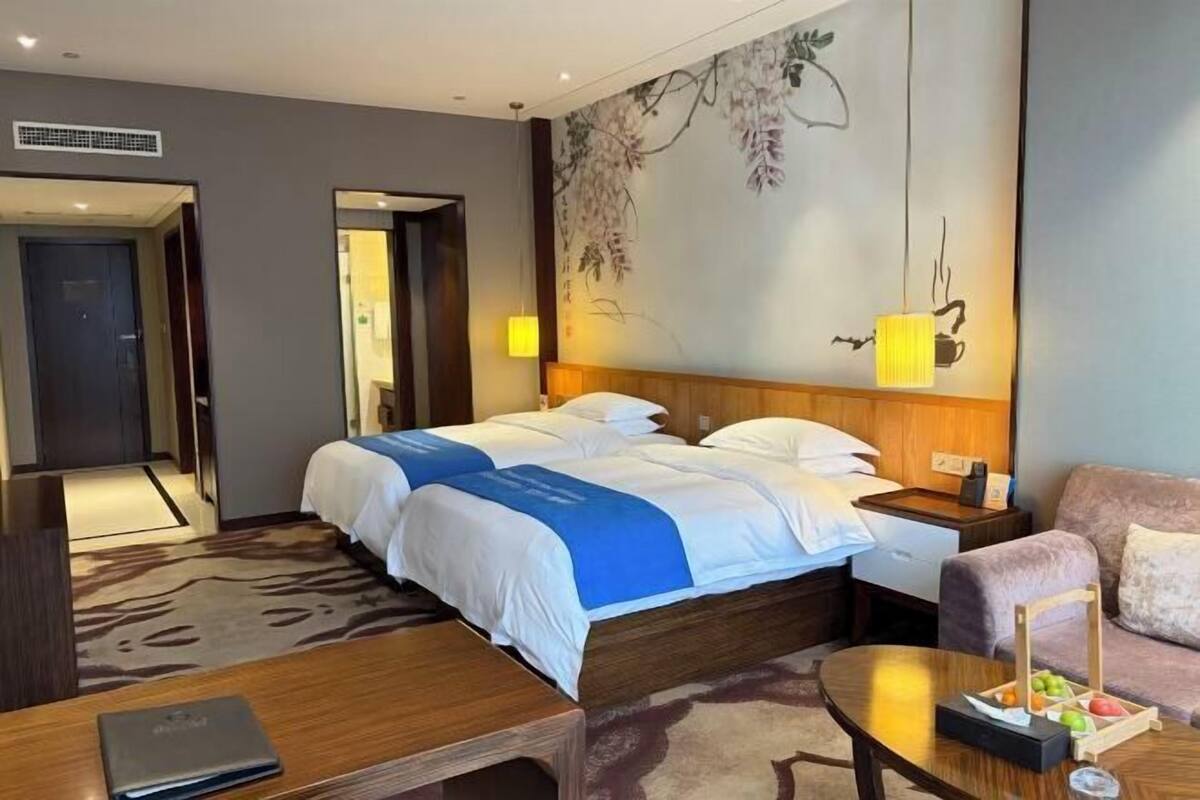 Habitación de hotel con una cama grande, un escritorio, una silla, un sofá y una pared con un mural floral.