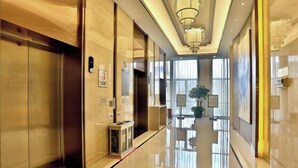 Un couloir d’hôtel moderne, avec un sol poli, des portes en verre et un lustre central.