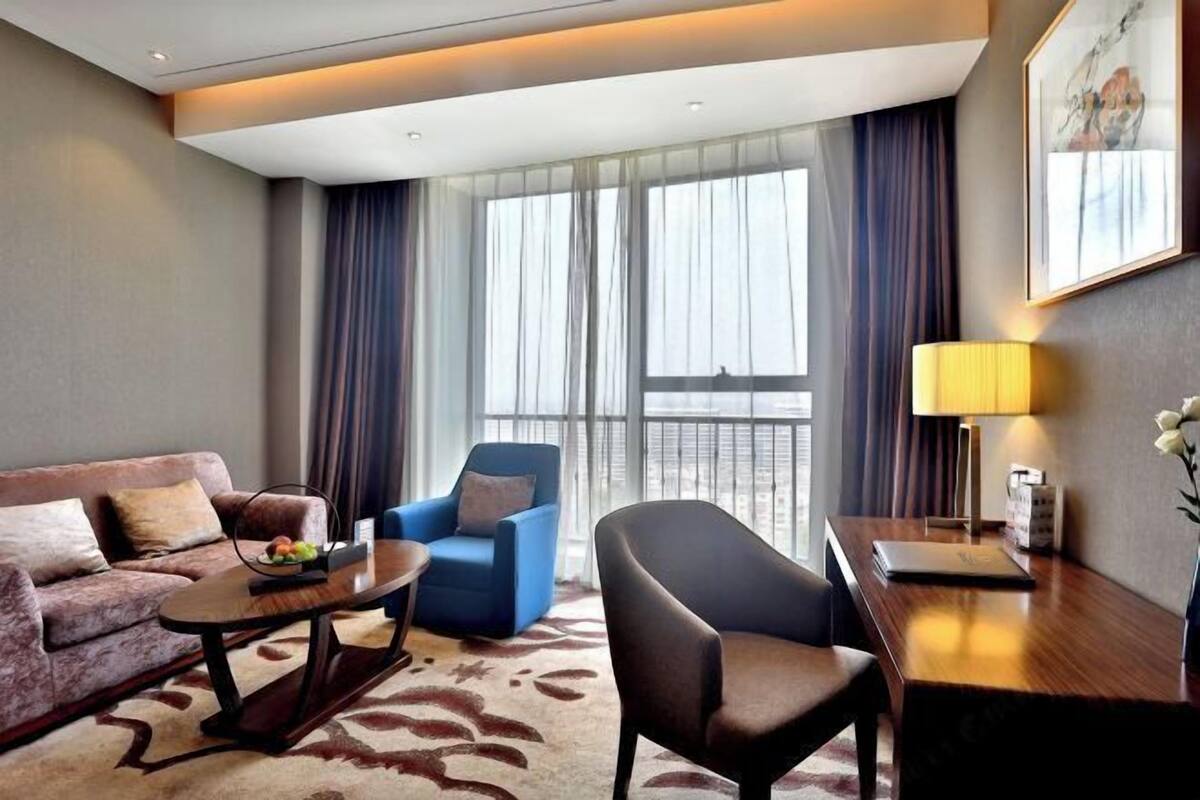 Una habitación de hotel con sofá, sillón, mesa de centro y escritorio con lámpara.