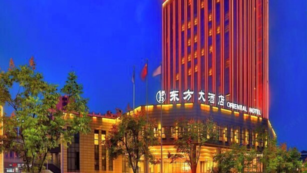 Un grand immeuble d’hôtel, doté d’une enseigne lumineuse, qui affiche notamment le nom « Oriental Hotel » en anglais et dans une autre langue.