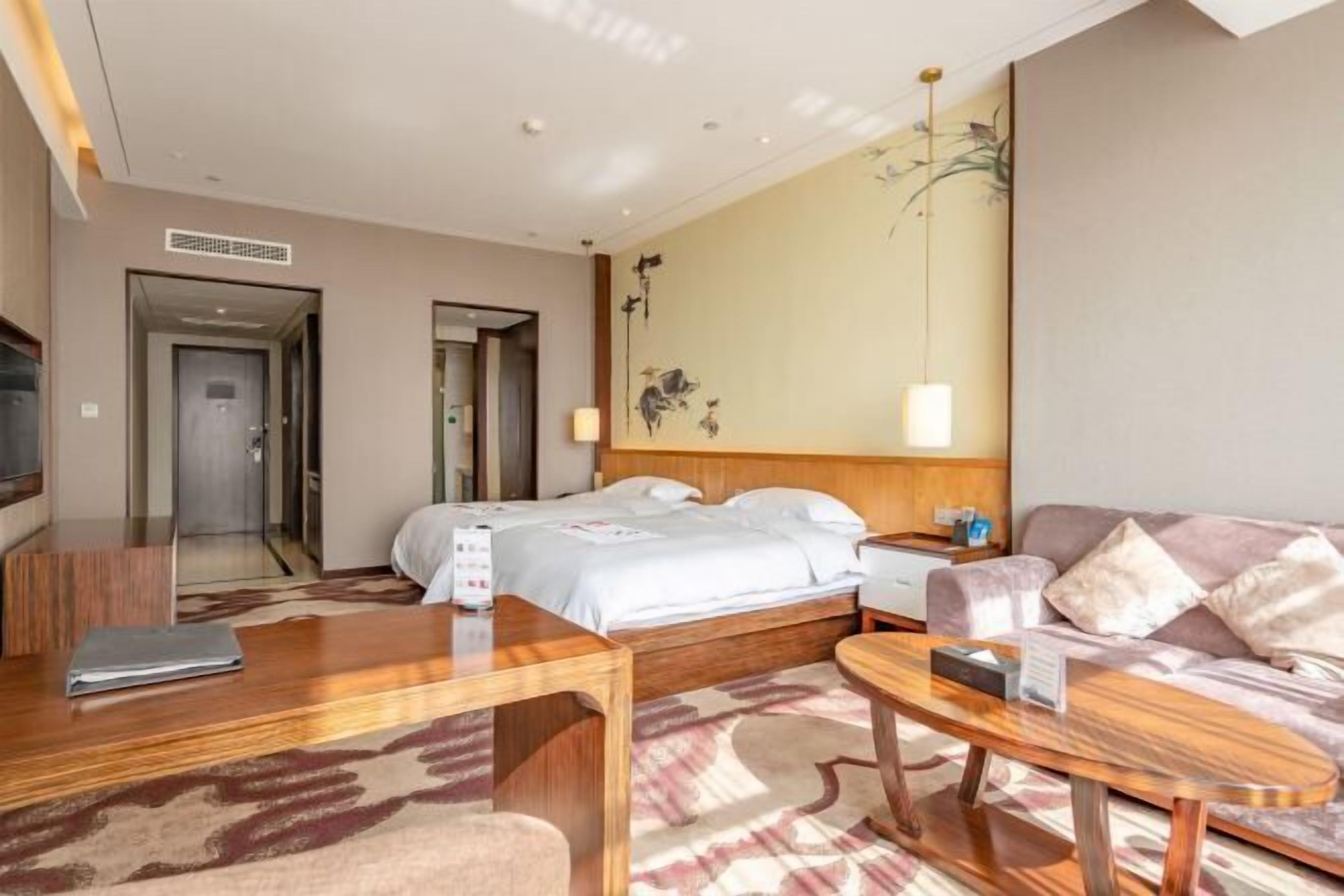 A hotel room with a bed, a desk, a sofa, a TV, and a wall with artwork.