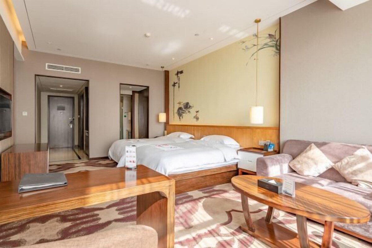 A hotel room with a bed, a desk, a sofa, a TV, and a wall with artwork.