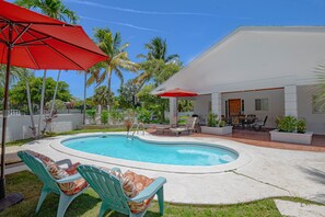 Une piscine entourée d’un patio aménagé, comprenant des chaises longues et des parasols.