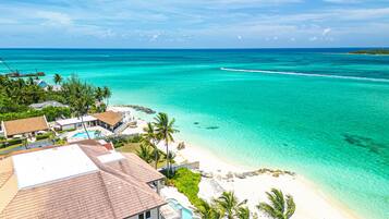 A tropical beach resort with a clear view of the ocean, a swimming pool, and a beach area with palm trees.