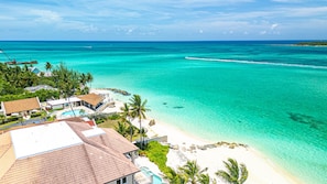 Un complexe hôtelier de style tropical situé sur une plage, offrant une vue dégagée sur l’océan, une piscine et un espace de plage agrémenté de palmiers.