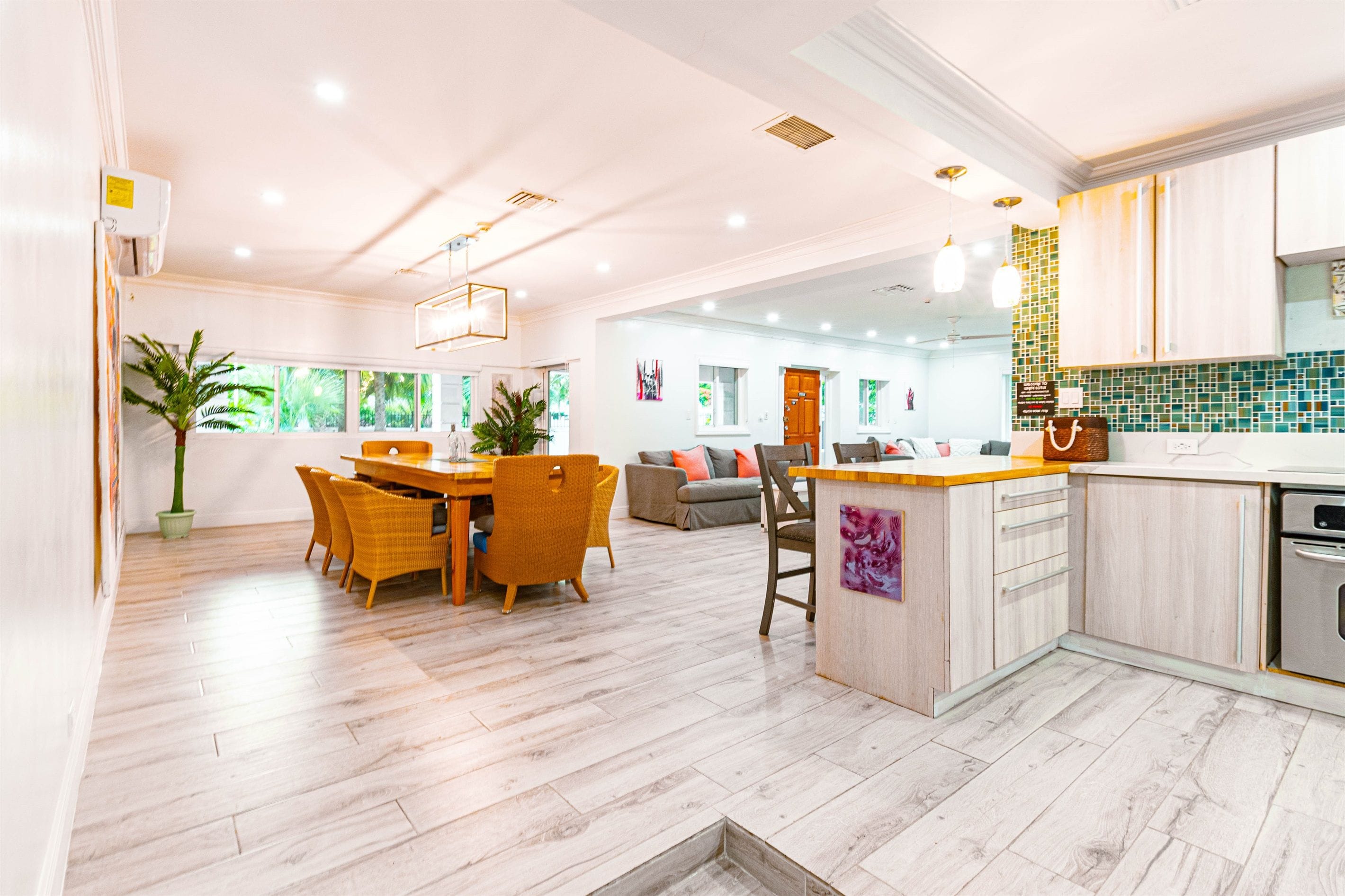 A modern kitchen with a central island, wooden flooring, and a dining area with wicker chairs.