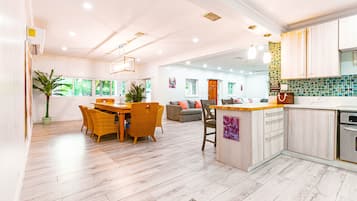 A modern kitchen with a central island, wooden flooring, and a dining area with wicker chairs.