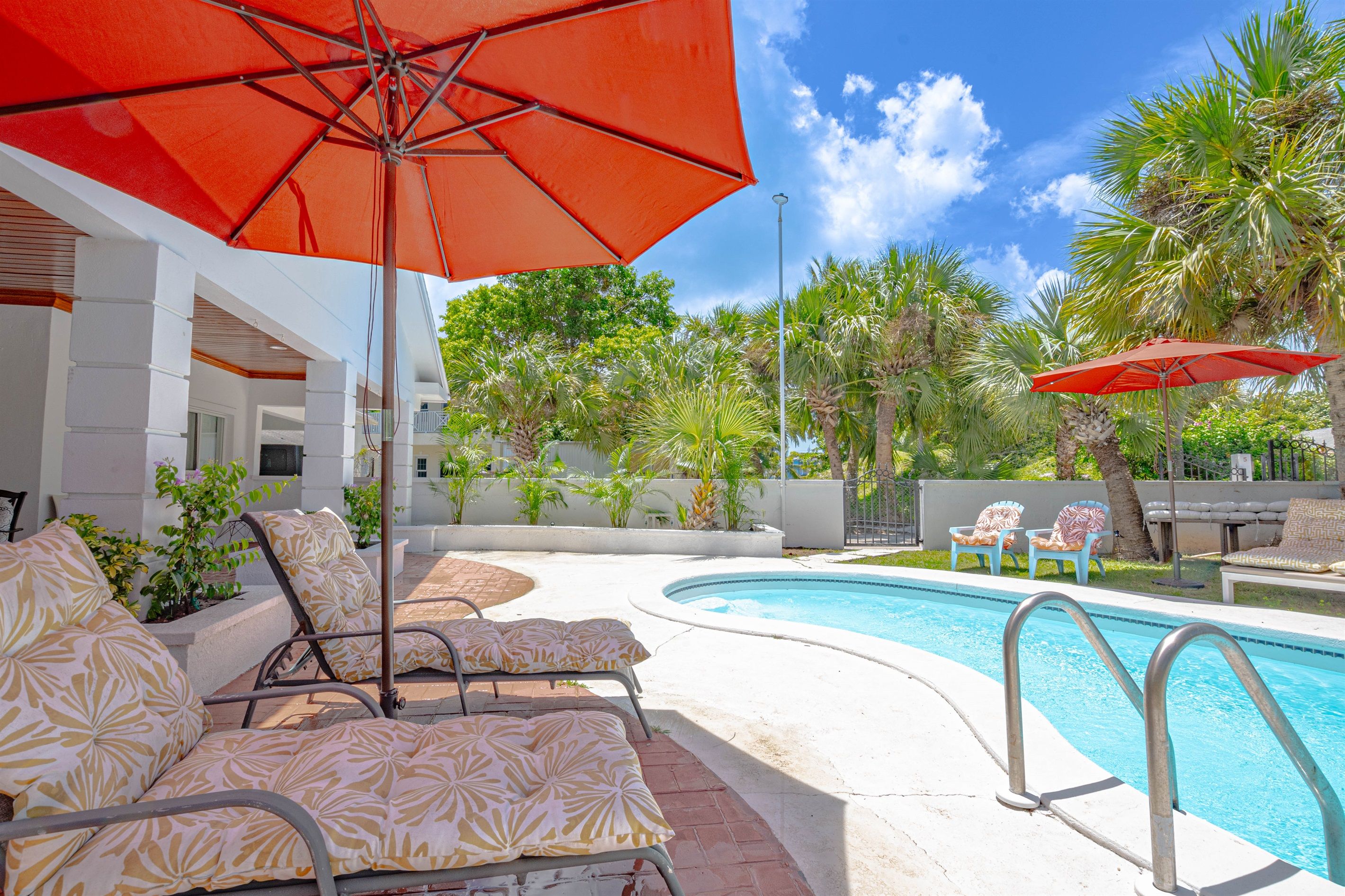 A poolside area with lounge chairs, an umbrella, and a clear blue sky.