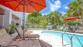 A poolside area with lounge chairs, an umbrella, and a clear blue sky.