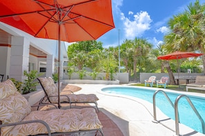 Un espace aménagé au bord de la piscine, avec des chaises longues, un parasol et un ciel d’un bleu limpide.